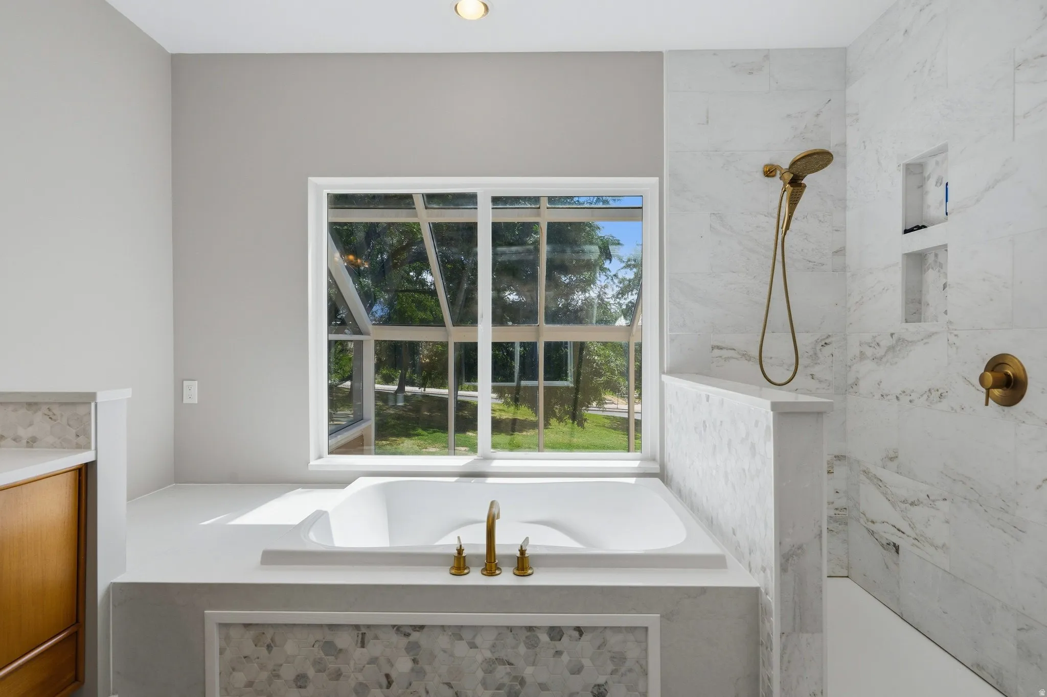 Built-in soaking tub with brass fixtures, large window, marble-look shower with brass showerhead, built-in shower niches, and recessed lighting