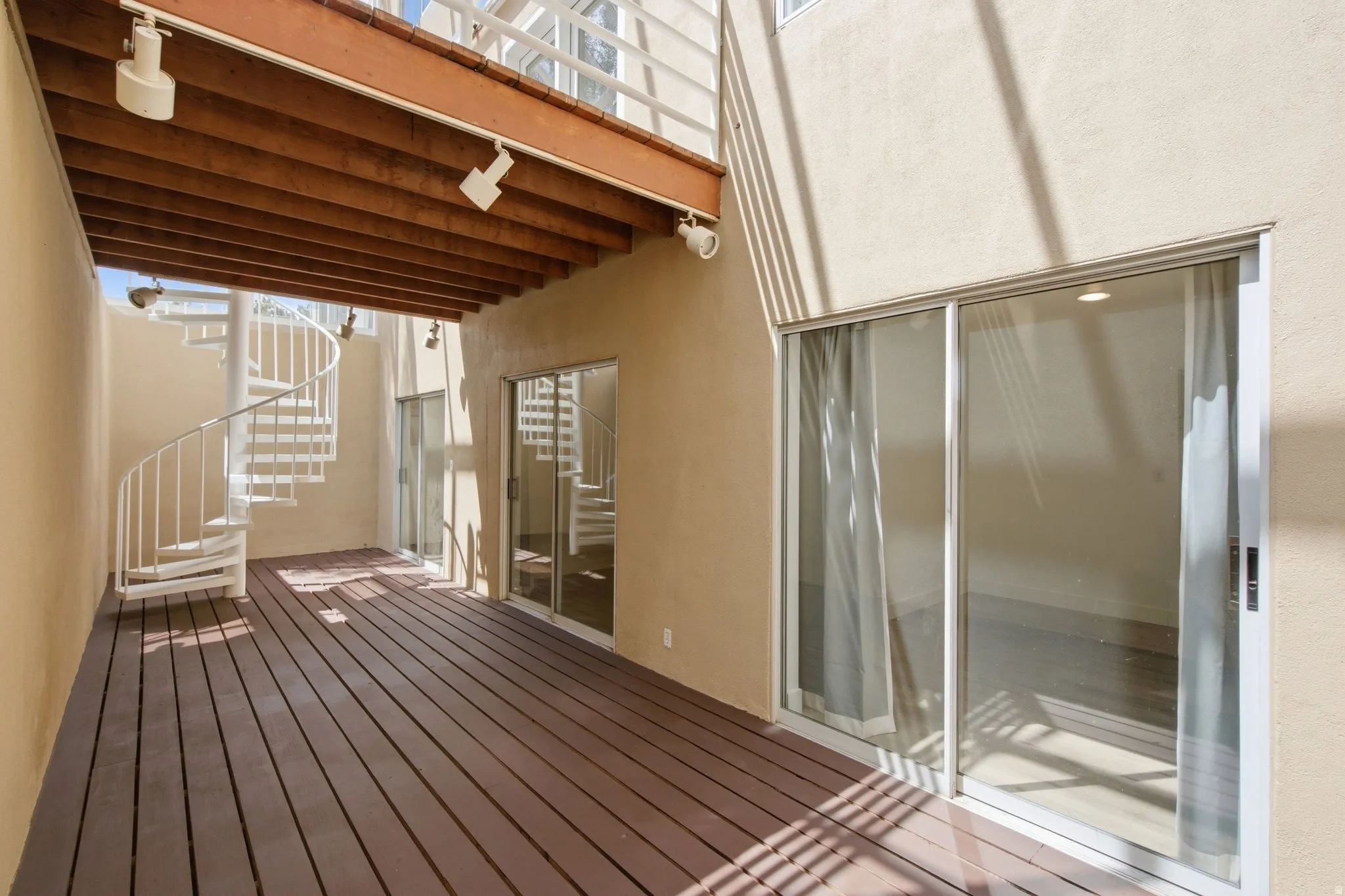 Expansive outdoor patio with dark wood-finish decking, a white spiral staircase, and multiple sliding glass doors