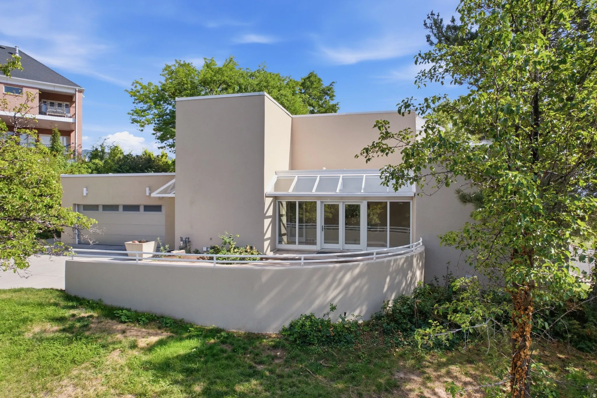 Modern architectural residence featuring clean geometric lines, expansive glass wall systems with integrated solar panels, rendered exterior walls, and mature landscaping with established trees framing the property