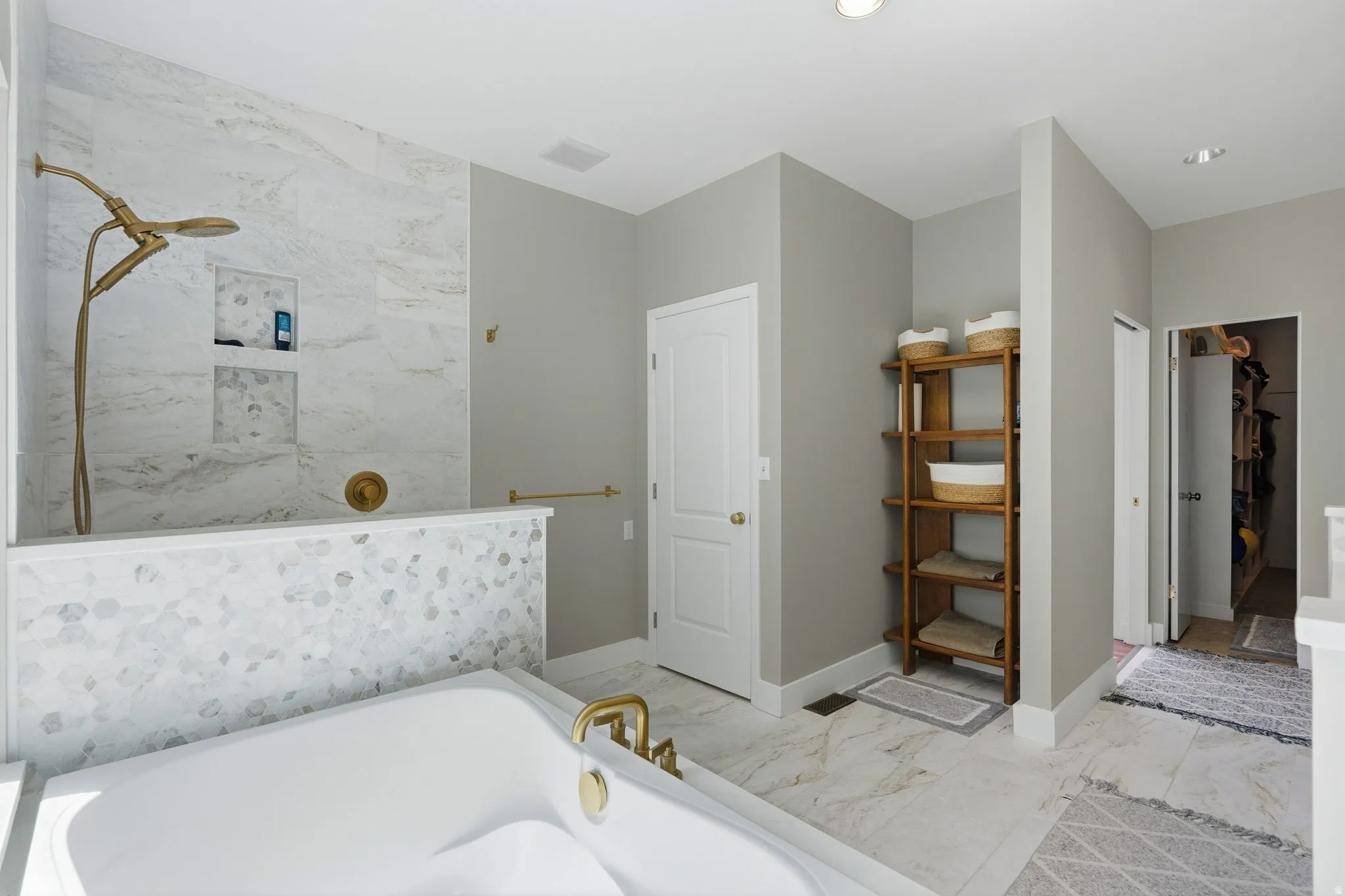 Freestanding soaking tub with brass fixtures, walk-in shower with natural stone tile and built-in niches, white solid-core doors, light-toned wall paint, and recessed lighting