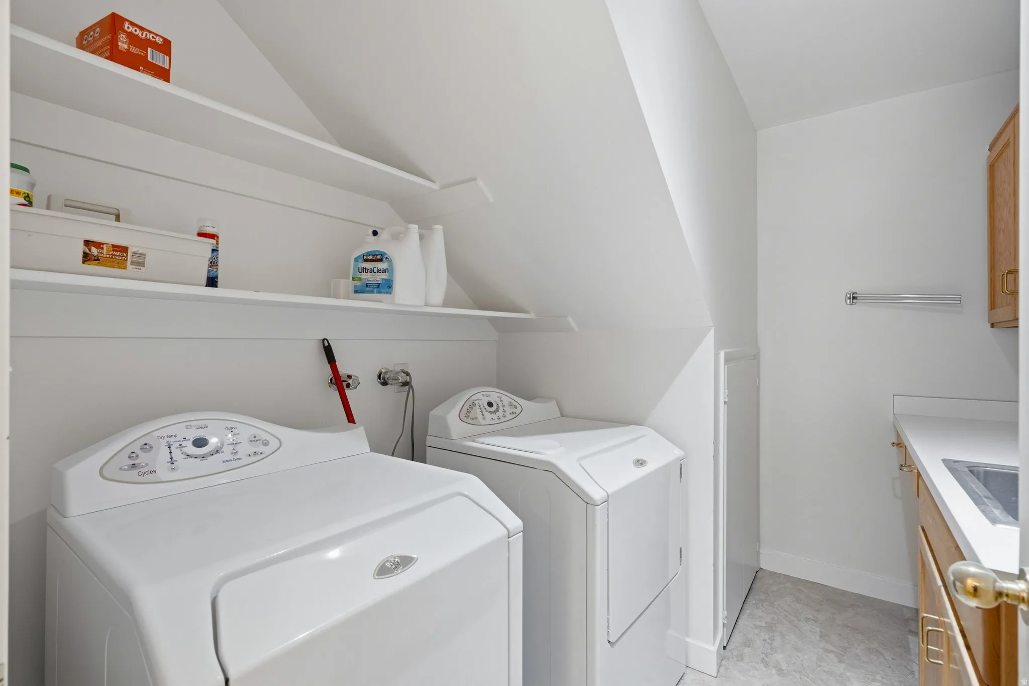 Dedicated laundry area featuring a built-in sink, wood-finish cabinetry, and overhead shelving