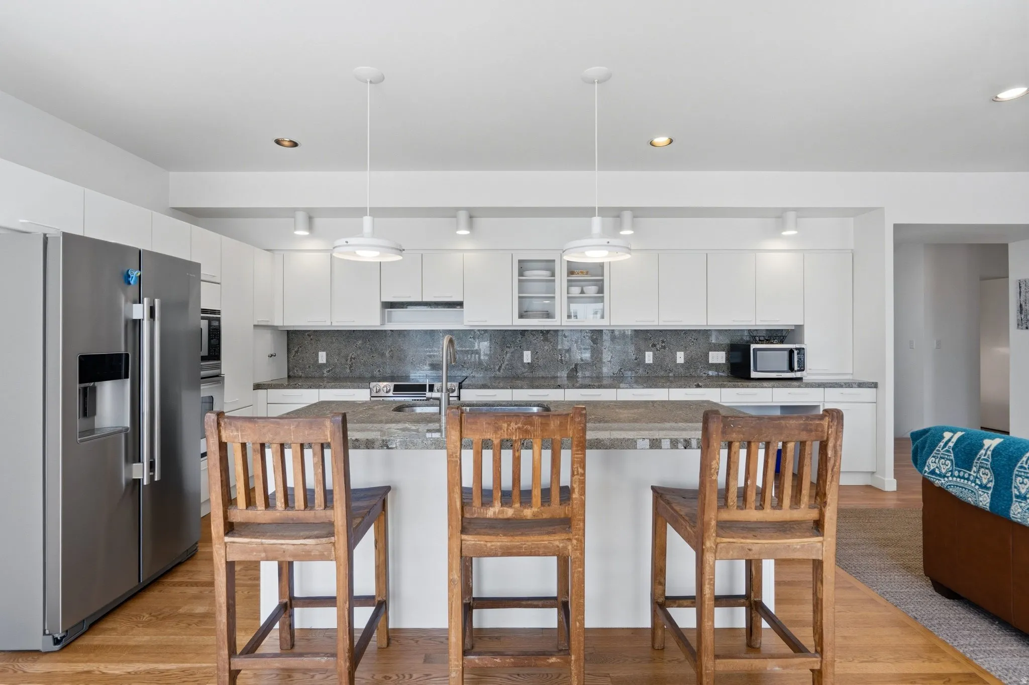 Kitchen featuring white flat-panel cabinetry, a stainless steel refrigerator, stone countertops, and a full-height stone backsplash