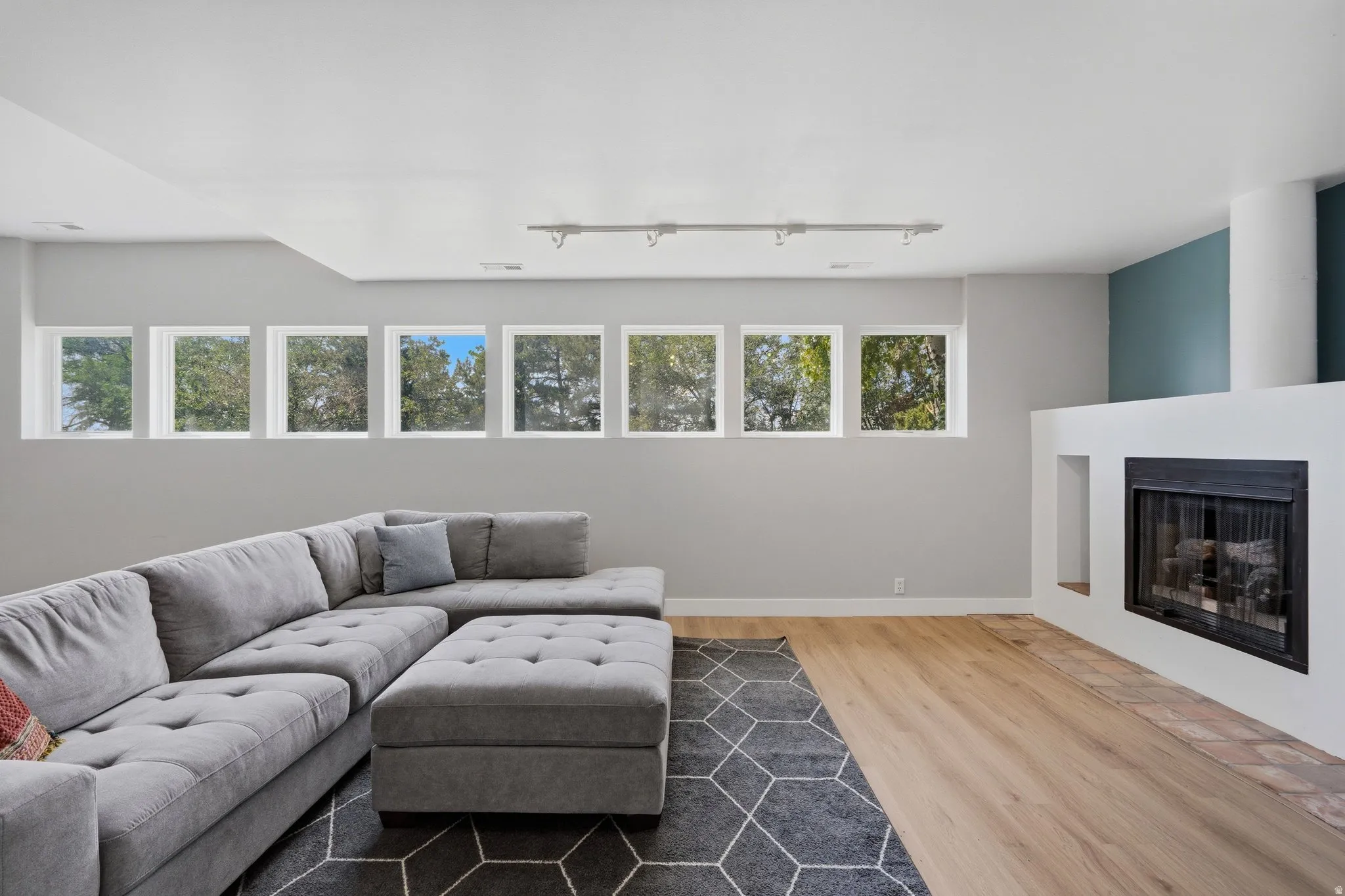 Wood-finish flooring, white fireplace surround, black firebox, multiple windows, and track lighting