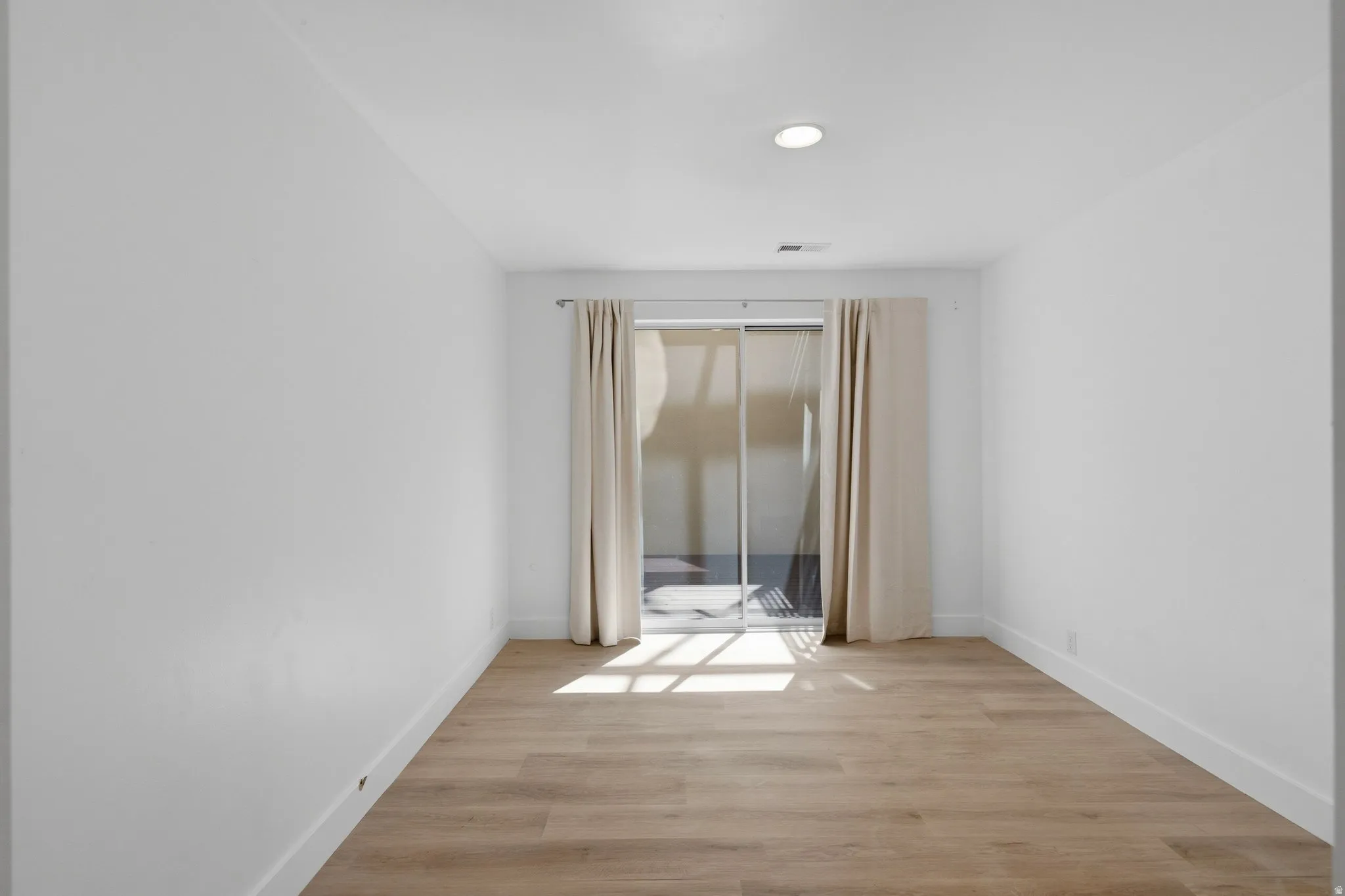 Wood-finish flooring, recessed ceiling light, white walls, and sliding glass door with drapes