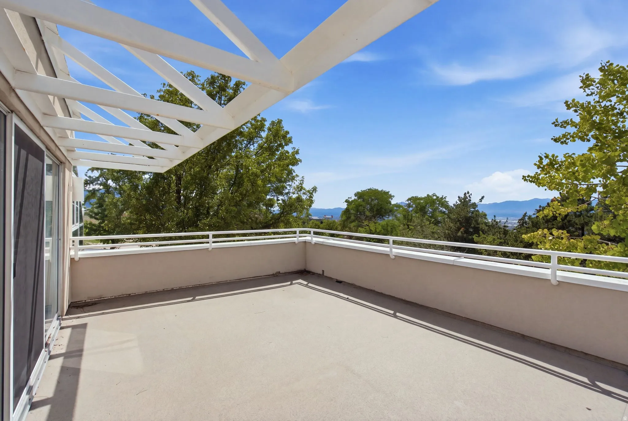 Expansive patio featuring a white metal railing, overhead pergola structure, and sliding glass door access