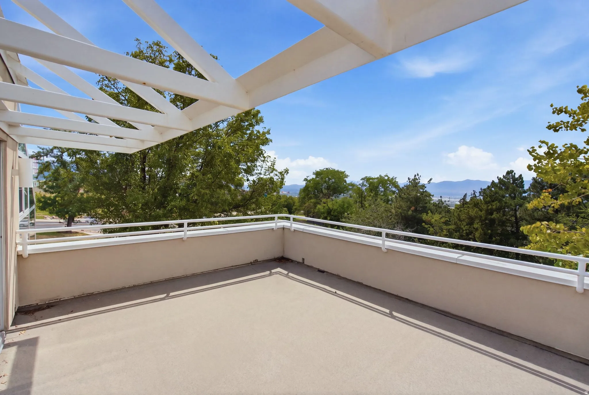 Expansive outdoor patio with a partial pergola, white railing, and a distant mountain backdrop