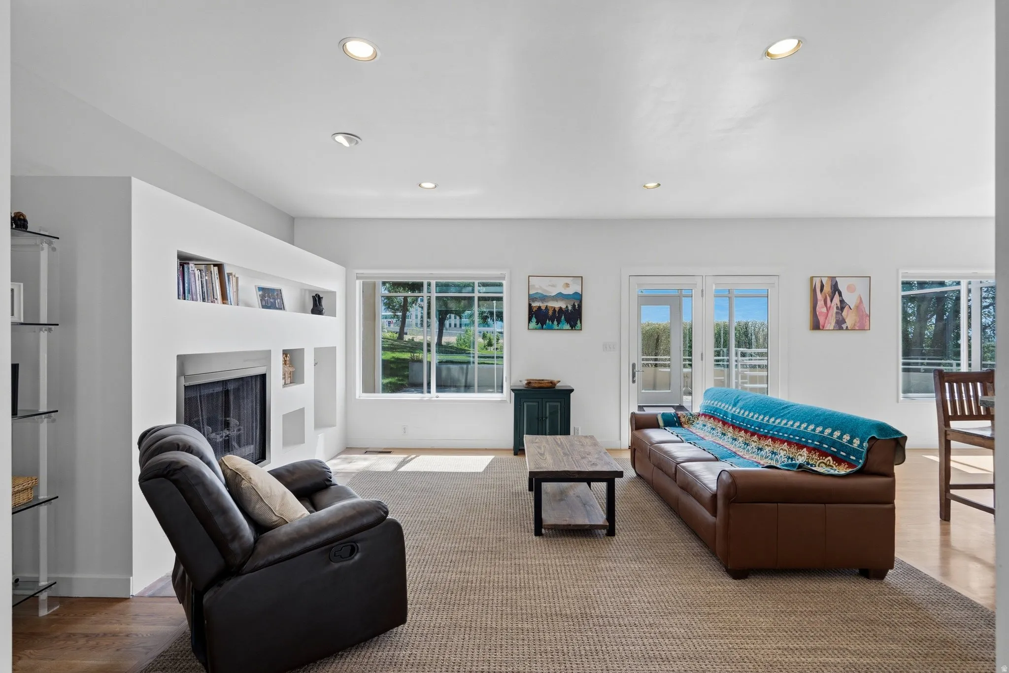 Recessed lighting illuminating a spacious room with a built-in fireplace, integrated shelving, and large windows