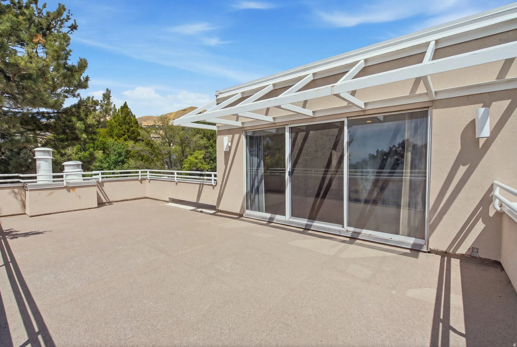 Expansive exterior terrace featuring sliding glass doors, a white metal awning structure, and modern wall-mounted lighting