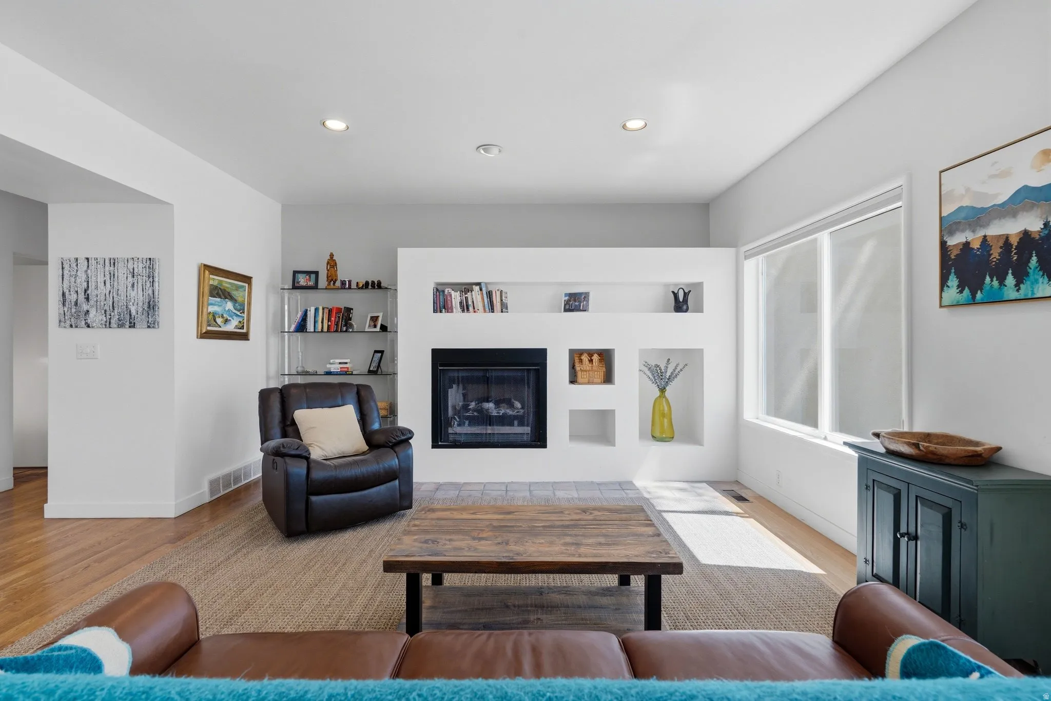 Bright, open living room showcasing gleaming wood-finish flooring, a custom built-in entertainment center with gas fireplace, and abundant natural light from large windows