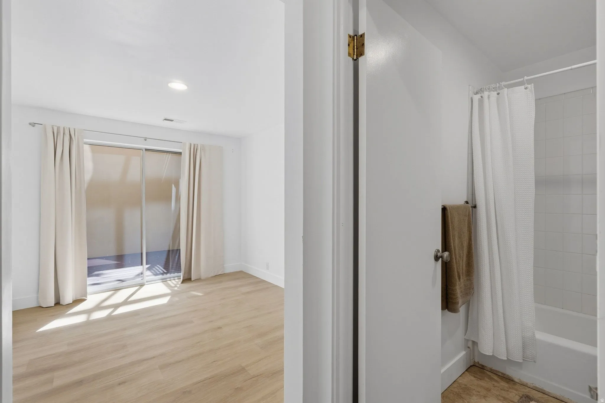 Recessed lighting, wood-finish flooring, sliding glass door, white wall finishes, and a full bathroom with a tiled shower surround