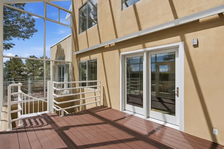 Expansive wood-finish deck with white railings, featuring full-light double doors and a glass enclosure