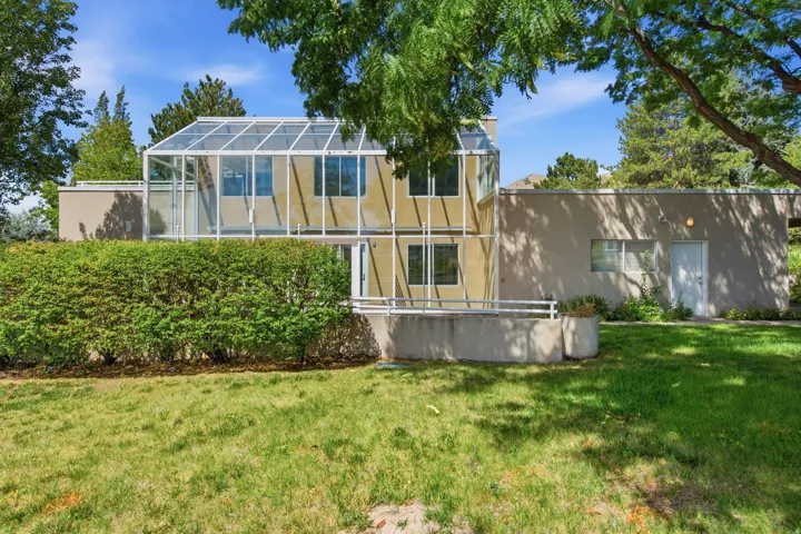 Two-story exterior with a glass enclosure, stucco finish, and mature hedge
