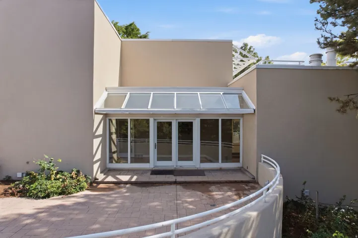 Modern architectural exterior with a glass-enclosed entry, multiple glass panel doors, and a decorative white railing