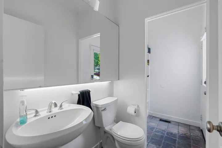 Pedestal sink with chrome-finish faucet, wall-mounted mirror with integrated lighting, and white toilet