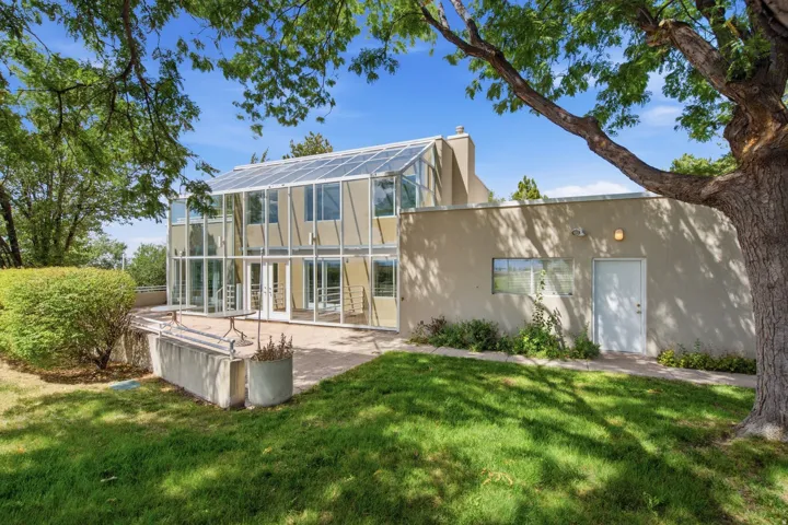 Modern residence featuring extensive glazing and clean-lined architecture, complemented by a mature shade tree and expansive lawn
