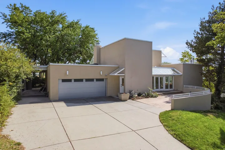 Modern stucco exterior with an integrated garage, concrete driveway, and a curving architectural wall