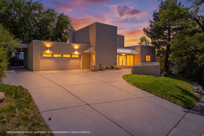 Modern architectural design with warm exterior lighting, a multi-panel garage door with horizontal windows, and an expansive concrete driveway