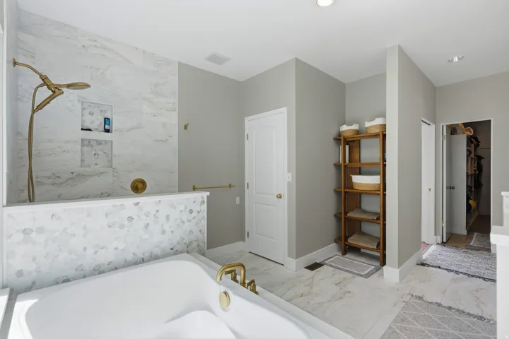 Freestanding soaking tub with brass fixtures, walk-in shower with natural stone tile and built-in niches, white solid-core doors, light-toned wall paint, and recessed lighting
