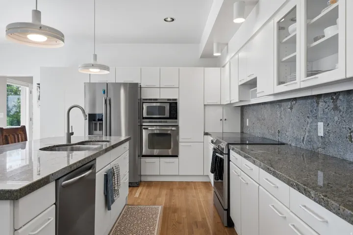 Contemporary kitchen with white cabinetry, stainless steel appliances, granite countertops, and wood-finish flooring