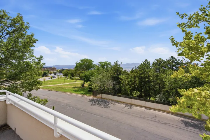 Balcony with painted railings overlooking a street, park space, and distant mountains