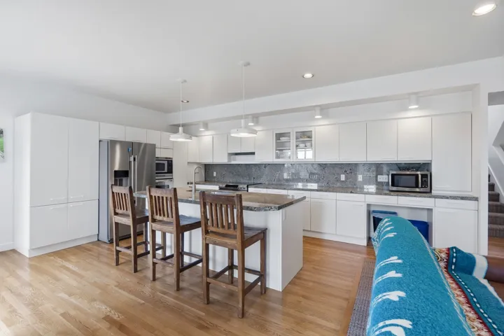 Sleek kitchen featuring wood-finish flooring, white cabinetry, stainless steel appliances, and a central island with a stone countertop