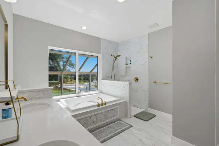 White stone-finish tile flooring complemented by a built-in soaking tub with gold-finish fixtures