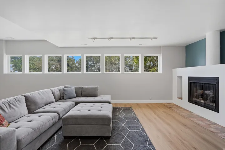 Wood-finish flooring, white fireplace surround, black firebox, multiple windows, and track lighting