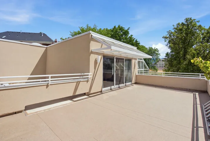 Expansive outdoor terrace featuring stucco walls, white railings, and mature trees