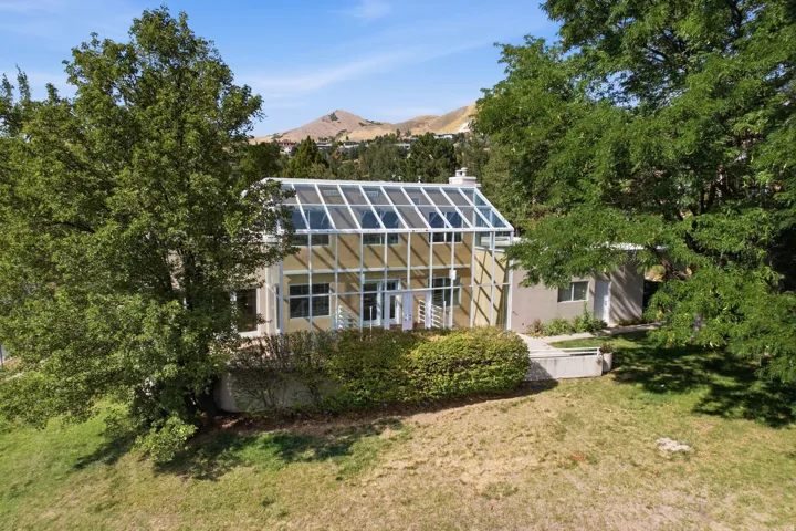 Contemporary exterior with a prominent glass-paneled roof structure, multiple levels, mature trees, and a terraced landscape