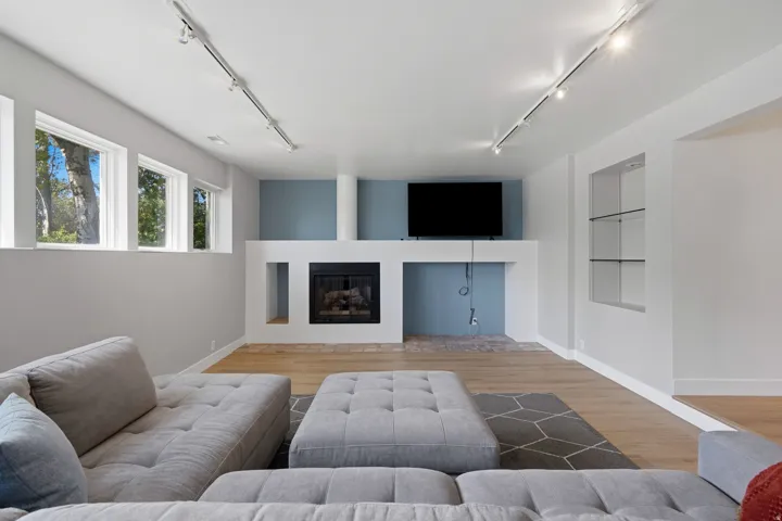 Built-in fireplace with a hearth, display shelving with glass shelves, track lighting, and wood-finish flooring