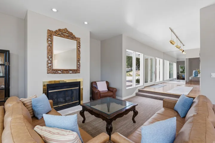 Recessed lighting, a fireplace with a brass surround, a large decorative mirror, and a wall of windows