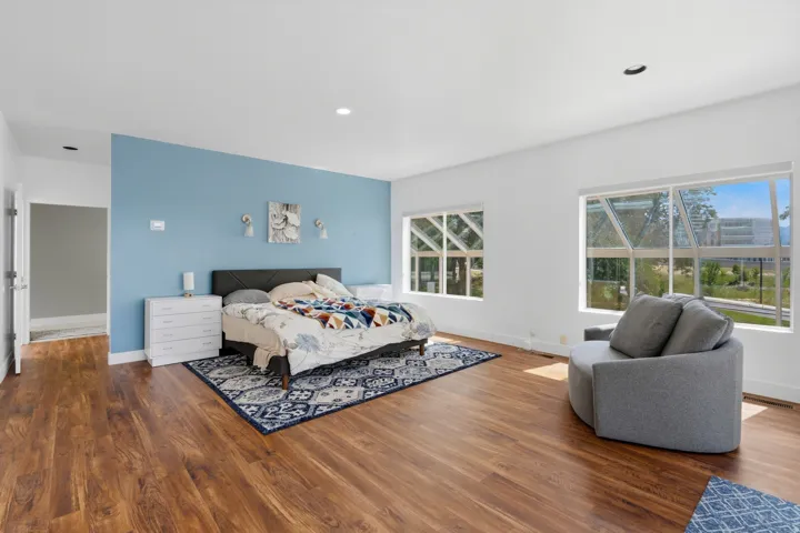 Spacious room featuring wood-finish flooring, a prominent blue accent wall, and multiple large windows