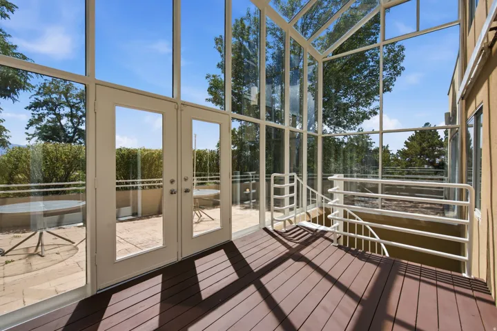 Floor-to-ceiling glass enclosure with French doors, composite decking, and white metal railings