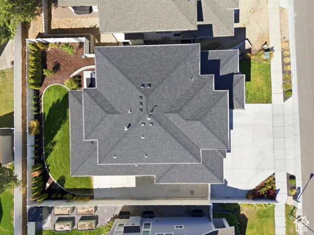 Pitched roof with gray shingles, concrete driveway, manicured lawn, and perimeter fencing
