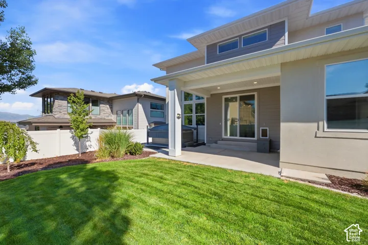 Expansive lawn with mature landscaping, covered patio, and large sliding glass doors