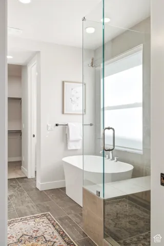 Freestanding soaking tub, glass-enclosed shower with tiled bench, recessed lighting, and large format floor tiling