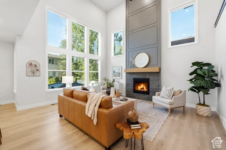 Double-height ceilings, a floor-to-ceiling fireplace with a wood mantle, light wood-finish flooring, and expansive windows