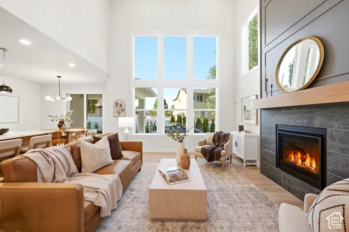 Two-story windows, fireplace with dark tile surround, light wood mantel, high ceilings, and wood-finish flooring