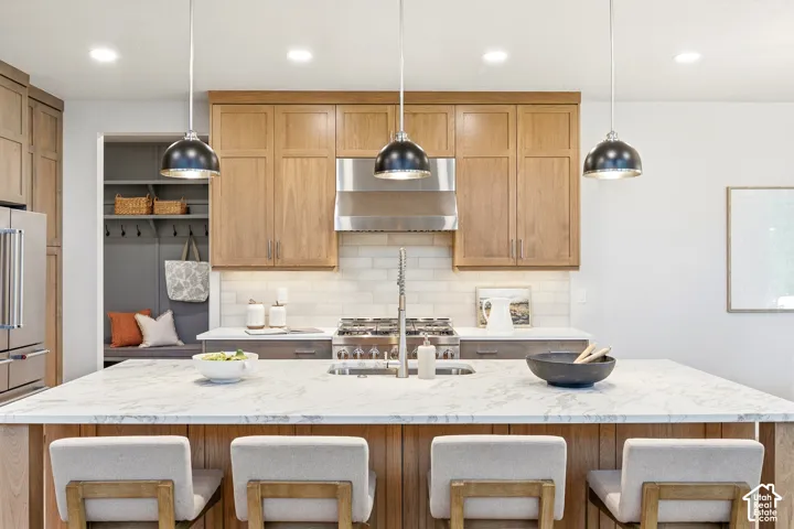 Expansive kitchen island with a light-toned countertop, stainless steel appliances, light wood-finish cabinetry, subway tile backsplash, and recessed lighting