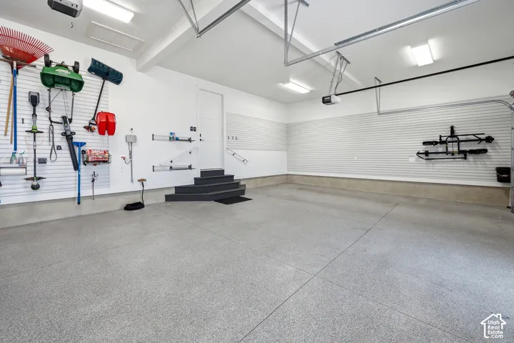 Spacious garage featuring a durable epoxy floor finish, organized slatwall storage systems, a utility door, and overhead lighting