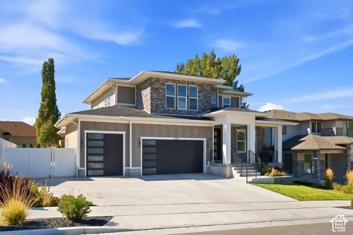 Contemporary architectural style featuring stone and siding exterior, a multi-car garage with modern doors, and a covered entry with white columns