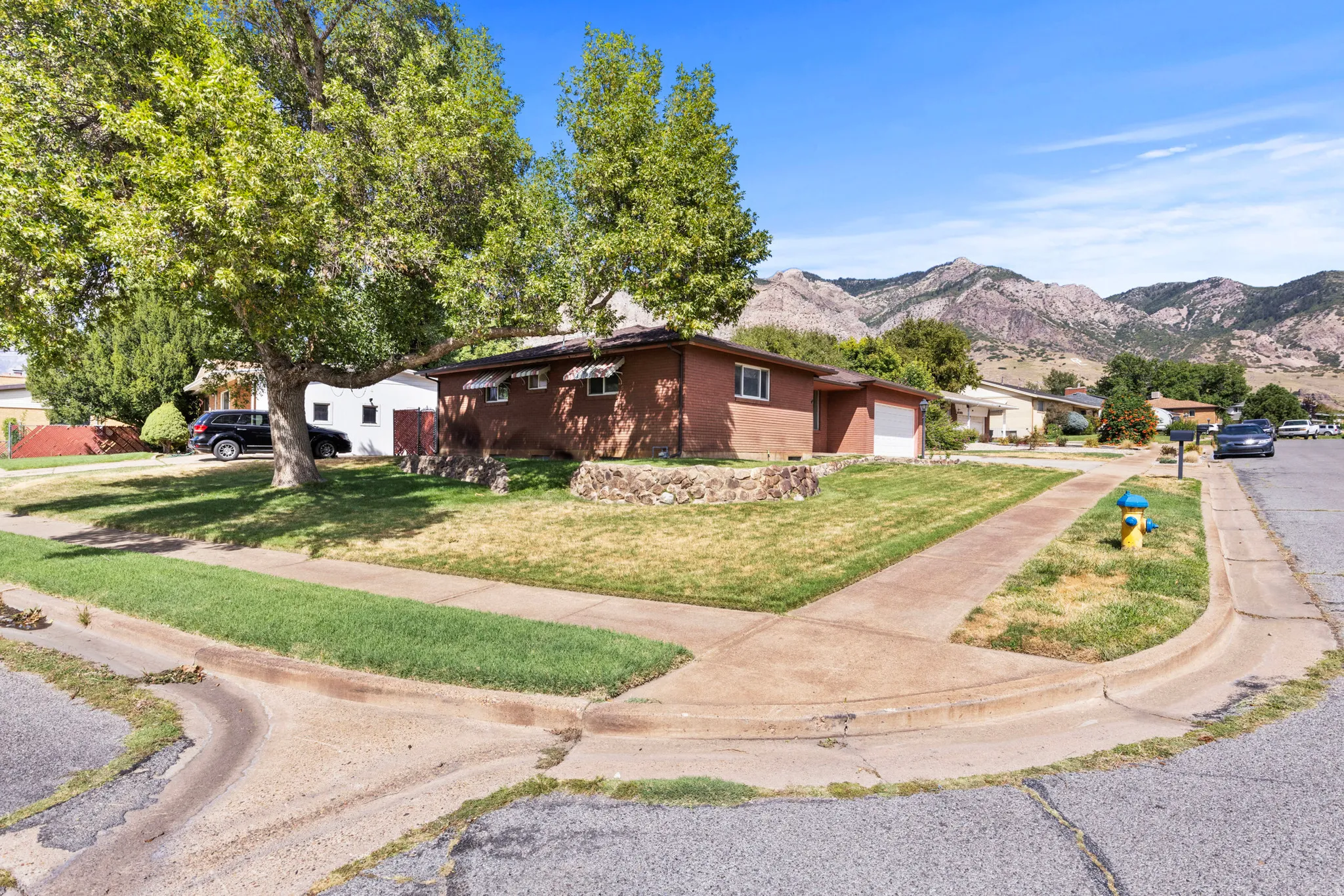 Brick exterior, attached garage, mature front yard trees, concrete driveway, mountain backdrop