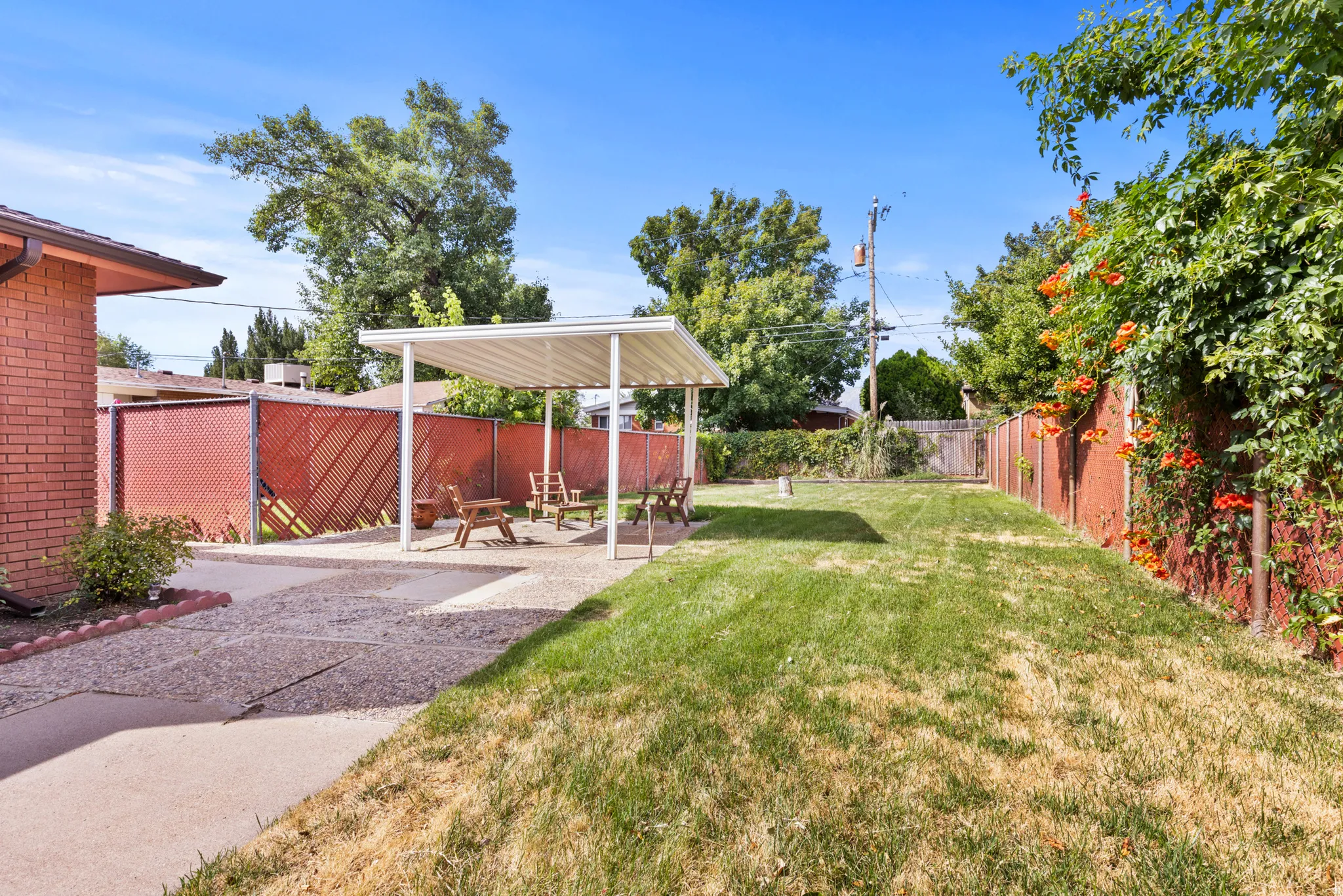Spacious backyard retreat featuring a manicured lawn, mature shade trees, and a covered patio structure with white framework
