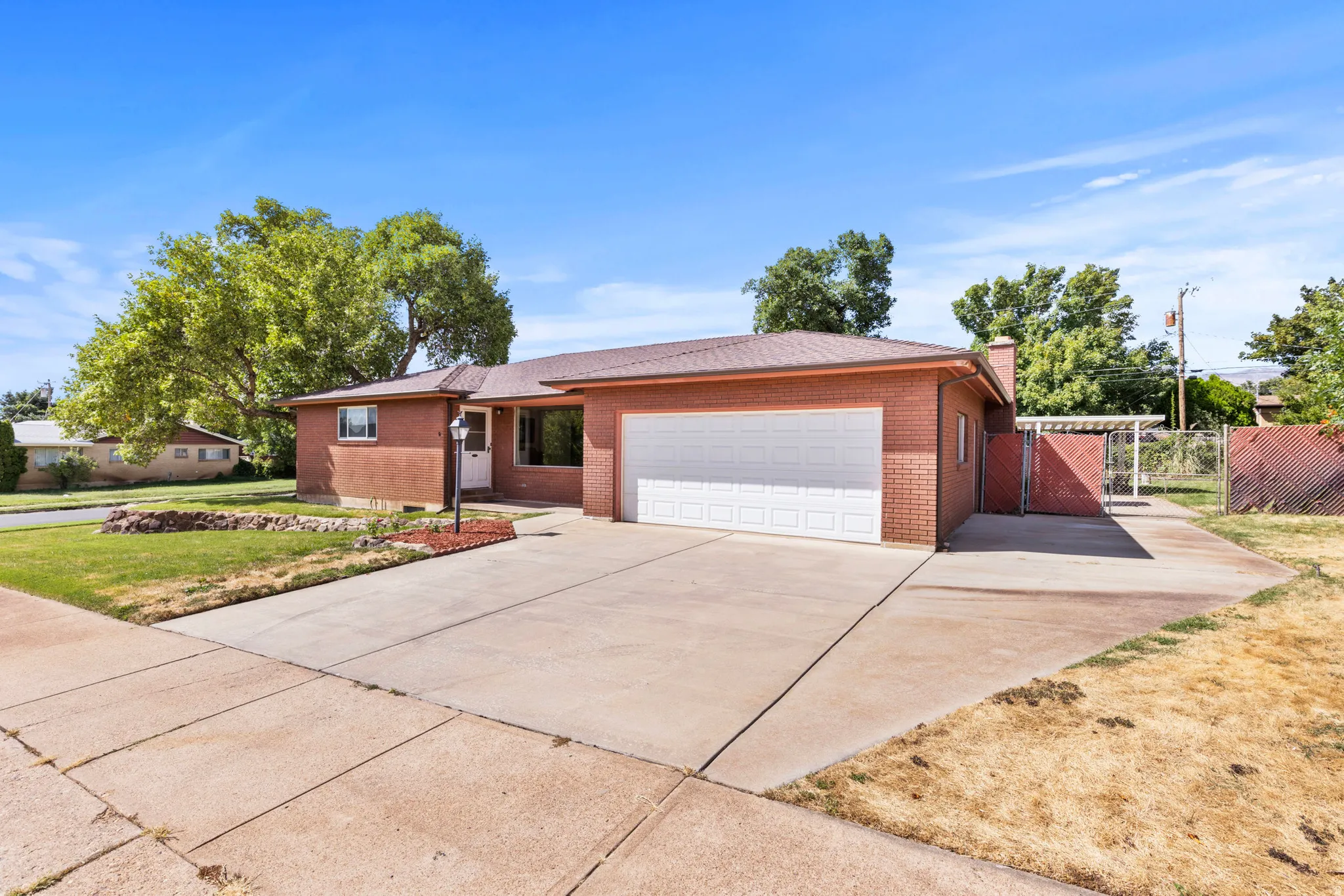 Brick exterior with a white garage door, concrete driveway, and a covered side patio