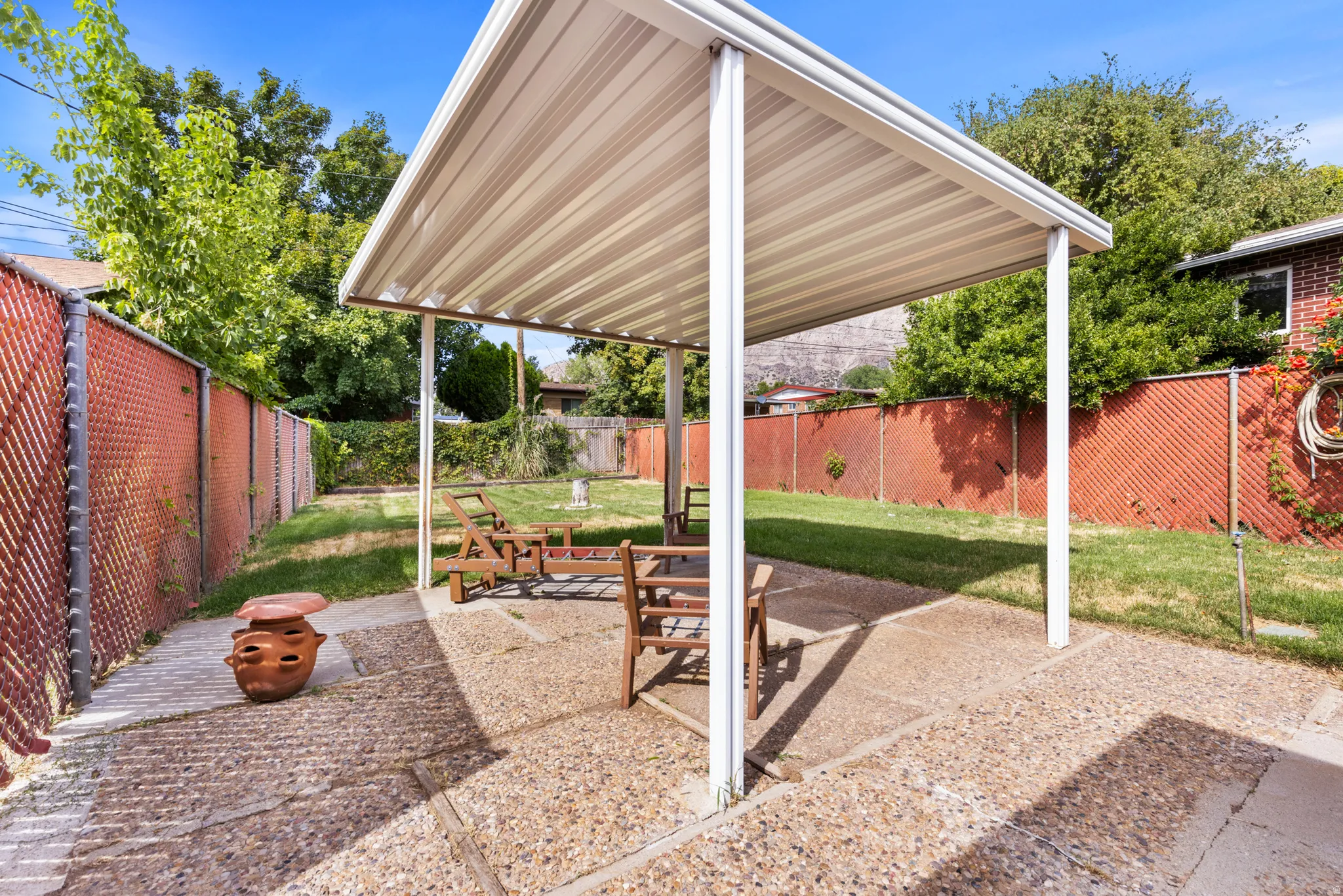 Covered patio with white support columns and overhead louvered roof providing shade over a gravel-surfaced entertaining space