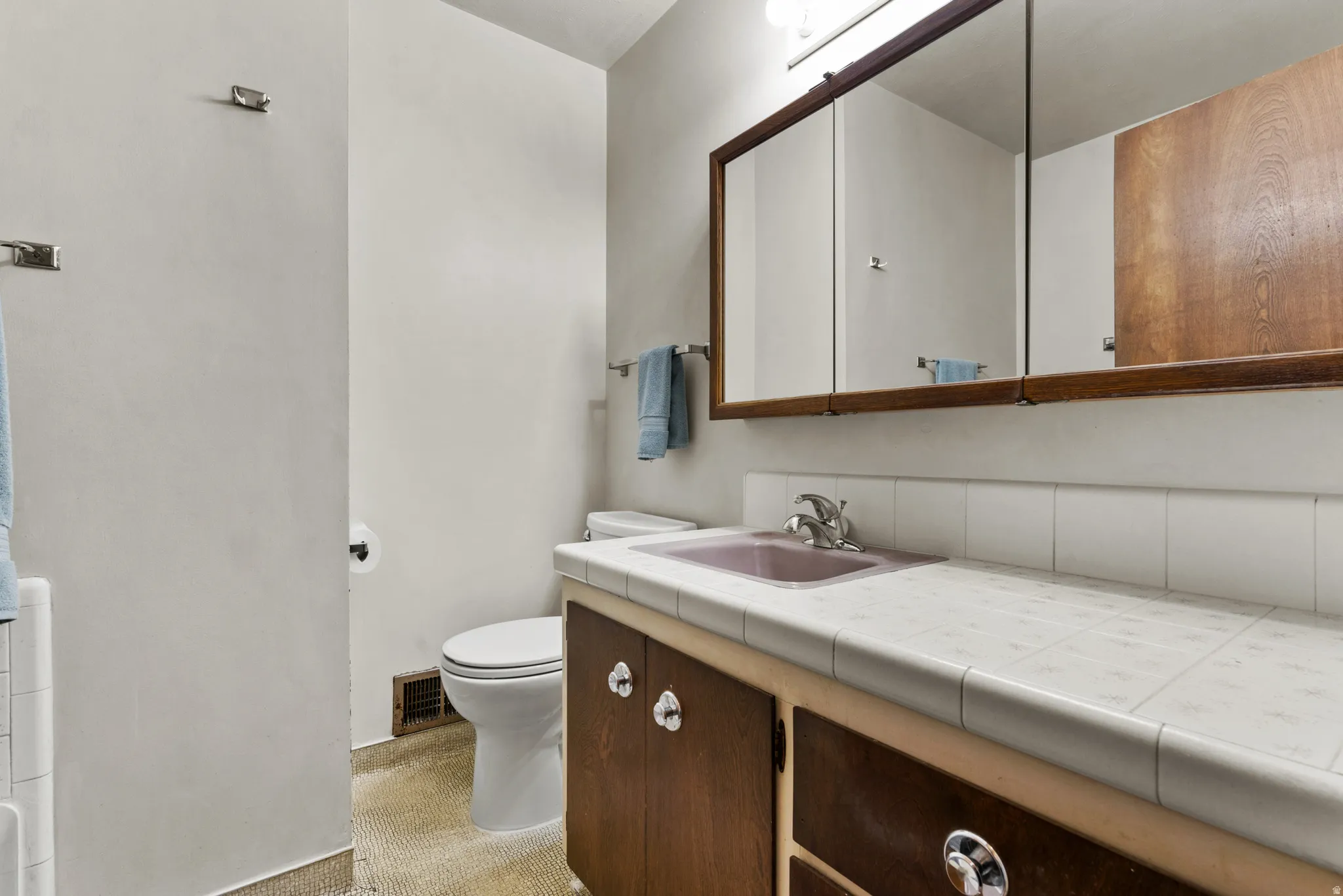 Spa-inspired bathroom featuring dual vanity with wood-finish cabinetry, white tile countertop, and polished chrome fixtures