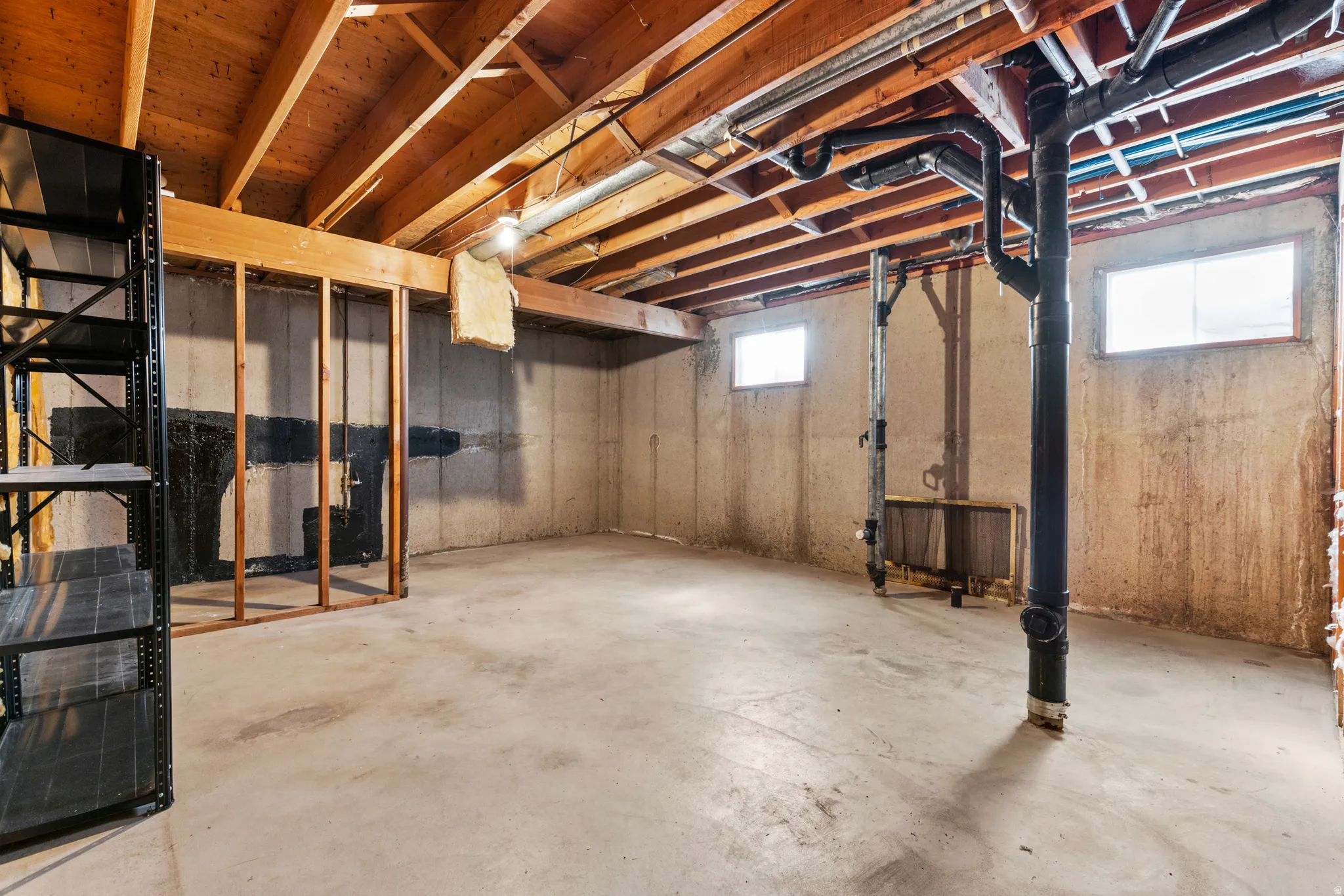 Unfinished basement featuring exposed wood joists, concrete foundation walls, concrete flooring, and multiple windows