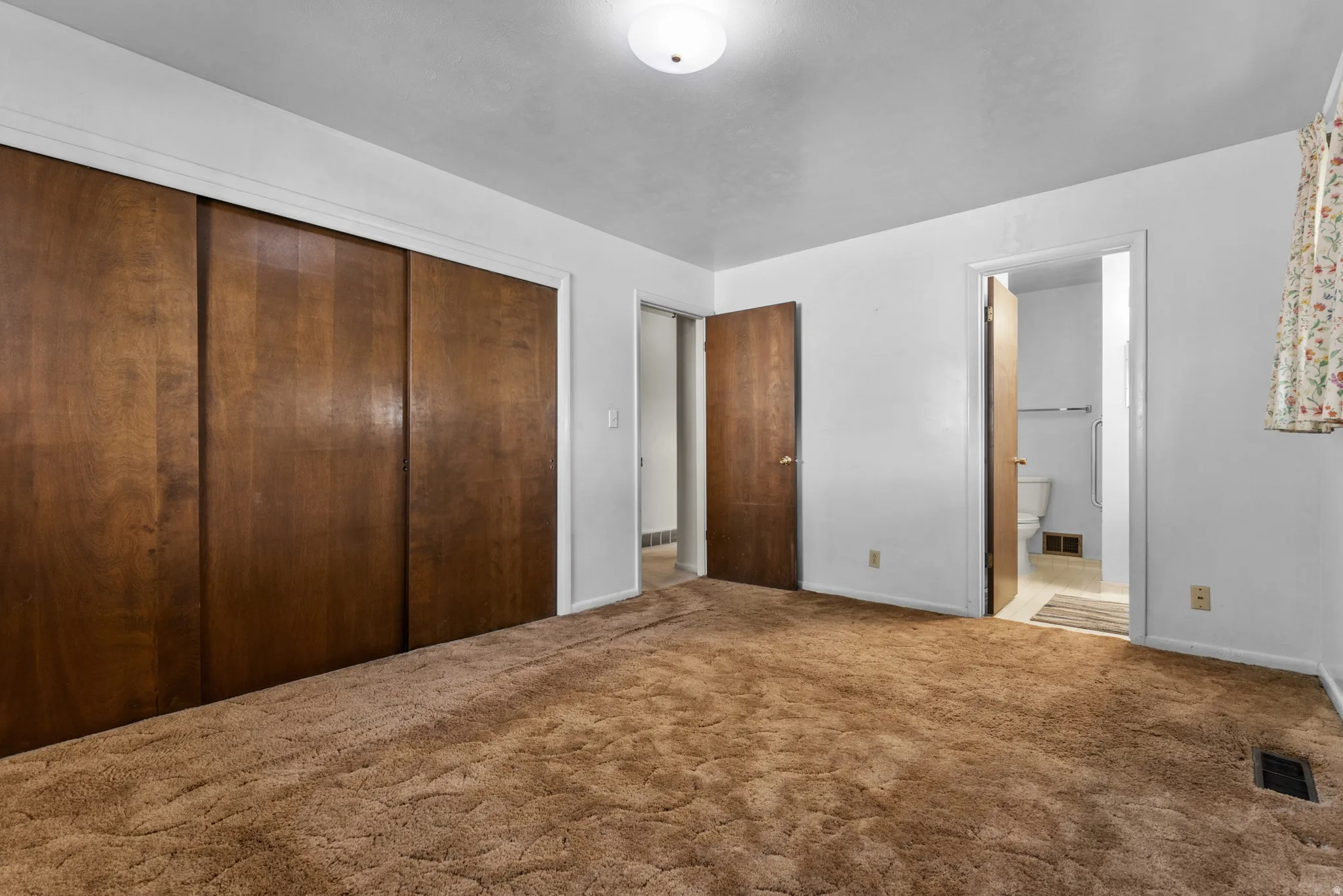 Spacious primary bedroom suite with triple wood-finish closet doors, neutral carpeting, and multiple entry points including direct access to an ensuite bathroom