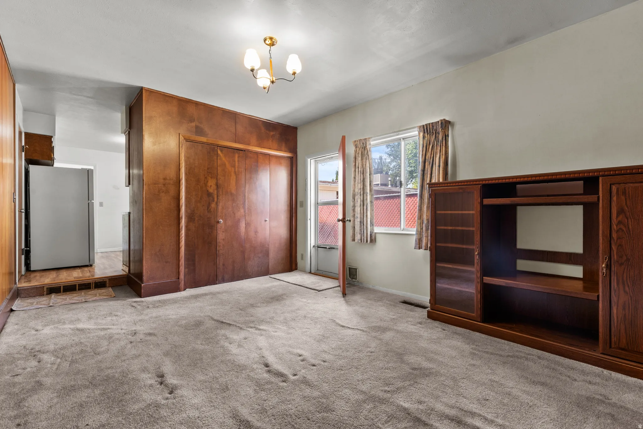 Spacious primary living area featuring original wood-finish cabinetry with built-in shelving, large closet storage with wood doors, carpet flooring, and abundant natural light from multiple windows