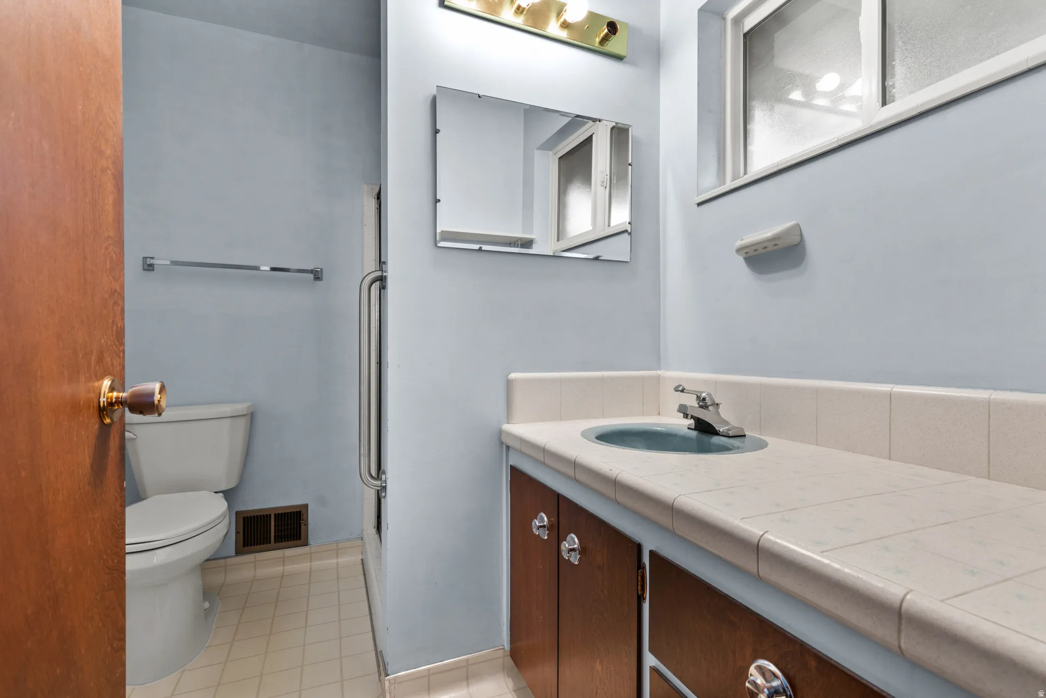 Spa-inspired bathroom featuring a wood-finish vanity with dual-sink configuration, ceramic tile countertop, and polished chrome hardware